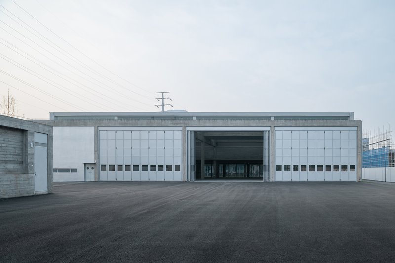 Symmetrical facade with sliding metal doors flanked by white panel walls beneath overhead power lines