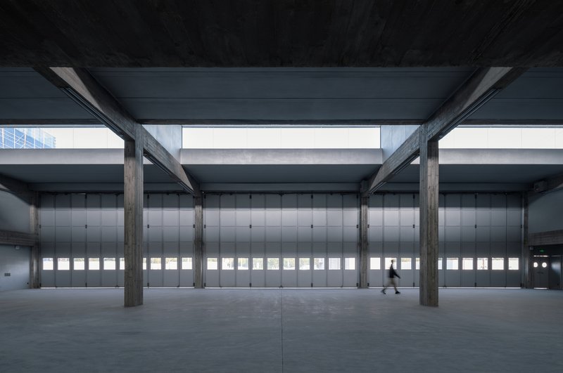 Covered arcade with exposed concrete columns and horizontal window bands in metal doors with one pedestrian