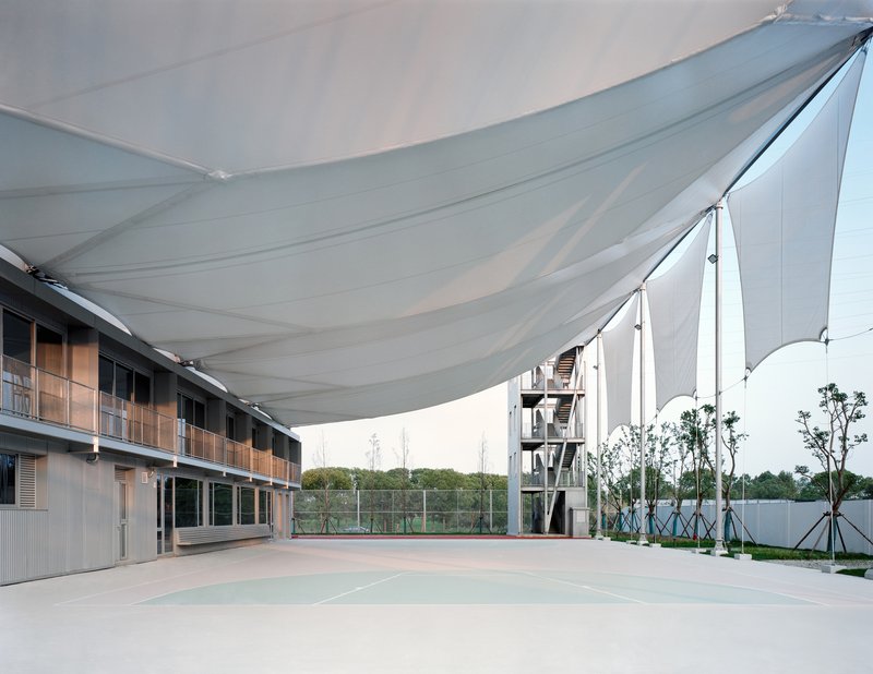 Courtyard with tensile fabric canopy stretched between residential blocks and a planted perimeter fence