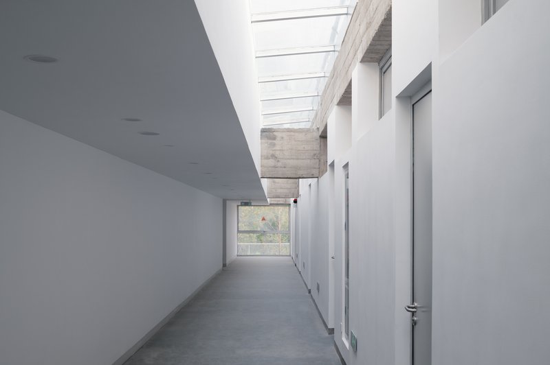 White interior corridor with linear skylight and exposed concrete beam under natural daylight