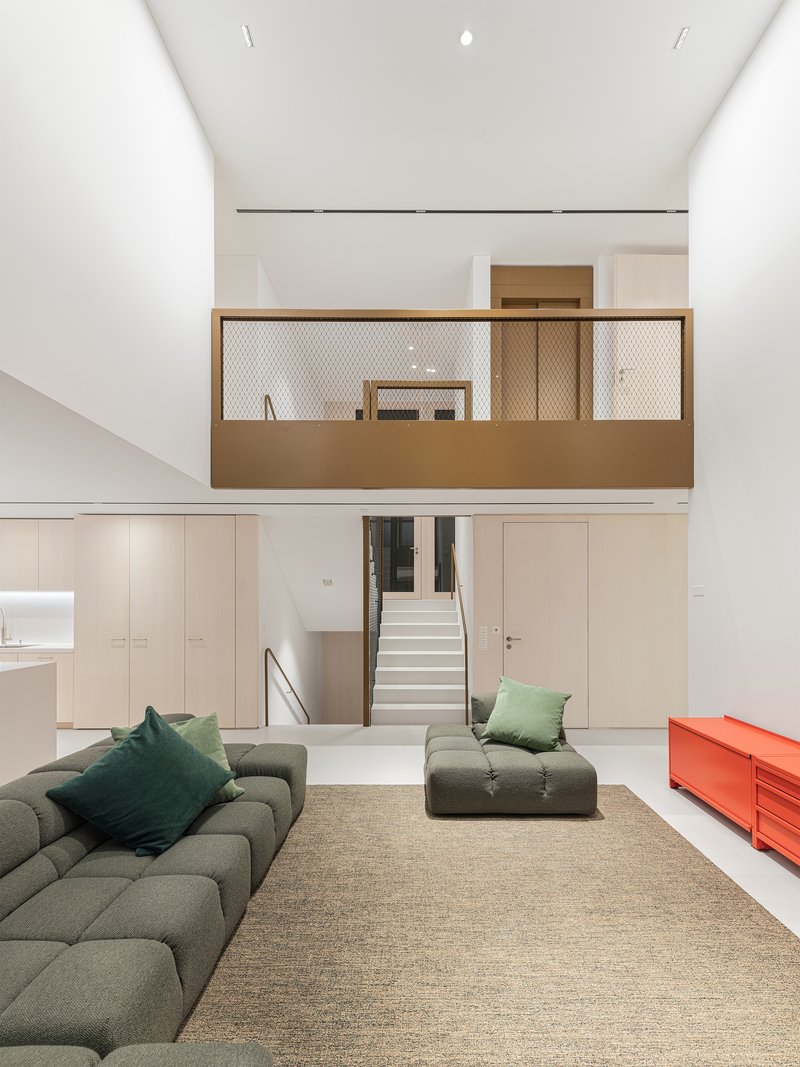 Double-height living room with suspended timber and mesh balcony above built-in storage and stair