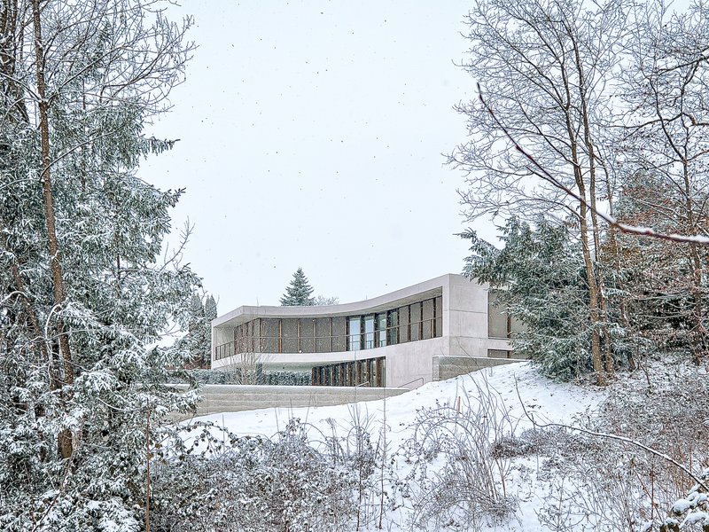 View of the curved concrete roof and timber screens from snow-covered garden with bare trees