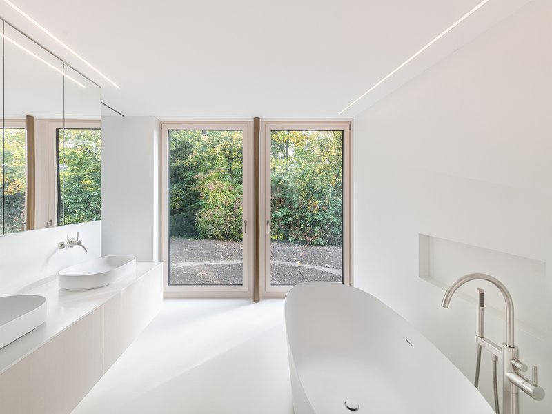 White bathroom with freestanding tub and timber-framed doors opening to garden with trees