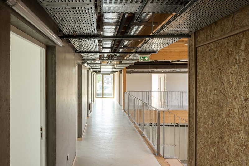 Interior corridor with exposed perforated metal ceiling, oriented strand board walls and steel guardrail overlooking lower level
