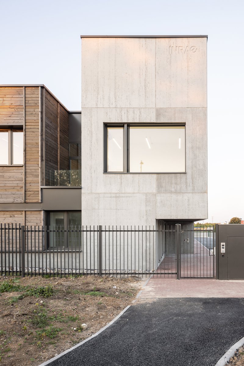 Street view of the concrete facade with a single window next to a timber-clad volume and metal fence