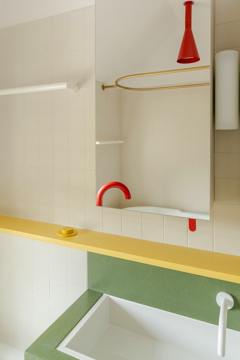 Bathroom vanity with yellow counter, green backsplash, red arched faucet and brass shower curtain rail