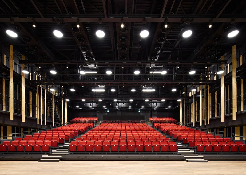 Stage view of auditorium showing symmetric rows of red seats and timber acoustic panels along both walls