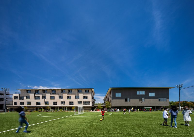 Two residential blocks flanking a sports field with children playing soccer on synthetic turf