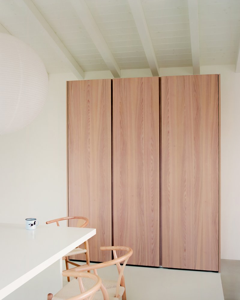 Floor-to-ceiling wardrobe in pale timber veneer beside a white dining table and timber chairs