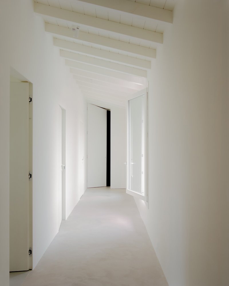 White hallway with exposed timber ceiling joists and open doorways leading to adjacent rooms