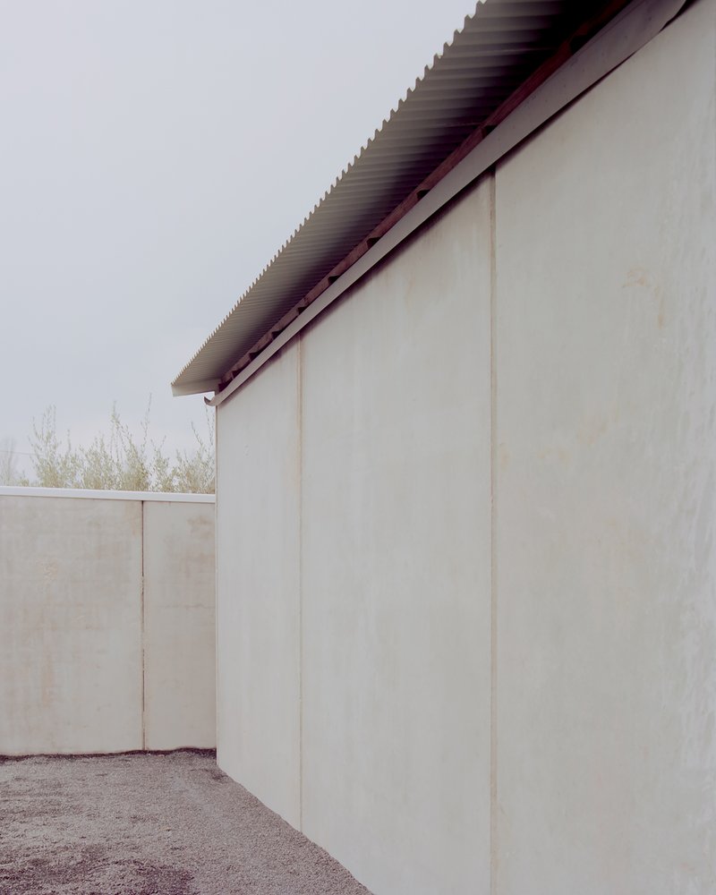 Corner detail of plastered walls with exposed corrugated metal roof eave under overcast sky