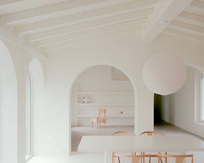 White interior with arched openings connecting dining and living spaces under exposed timber ceiling
