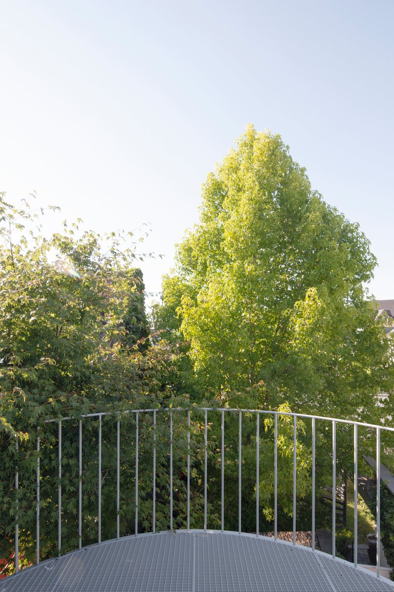 Curved terrace with metal balustrade overlooking trees under afternoon sunlight