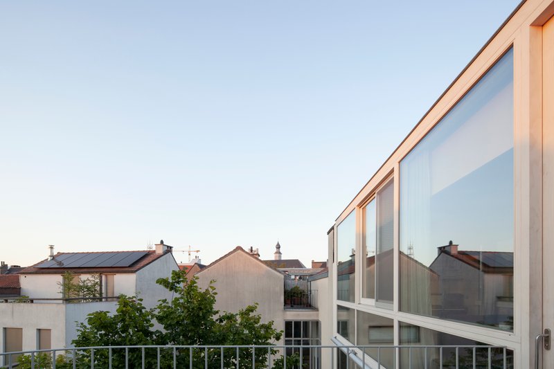 Timber-framed glazed upper level with white railing overlooking neighboring rooftops at sunset