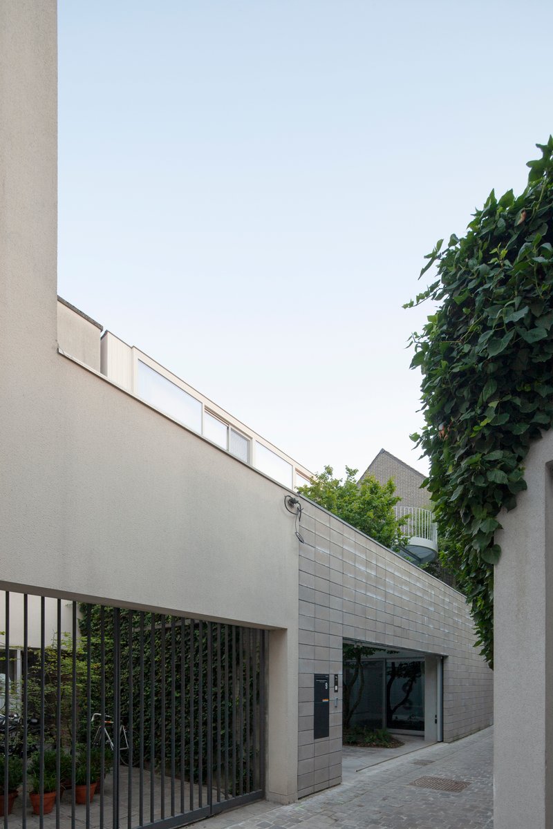 Street view of white block volumes and grey tile wall between ivy-covered neighbors