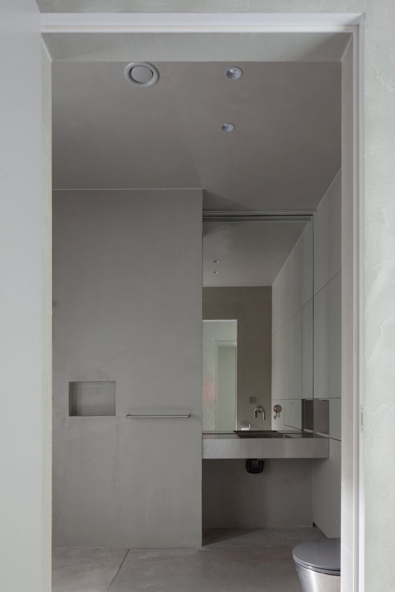 Compact bathroom with floating concrete sink and recessed niche seen through a white doorway