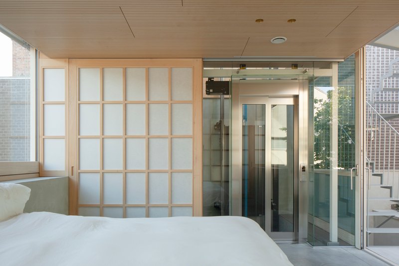 Bedroom with translucent sliding shoji screens and glass shower enclosure beneath a timber slatted ceiling