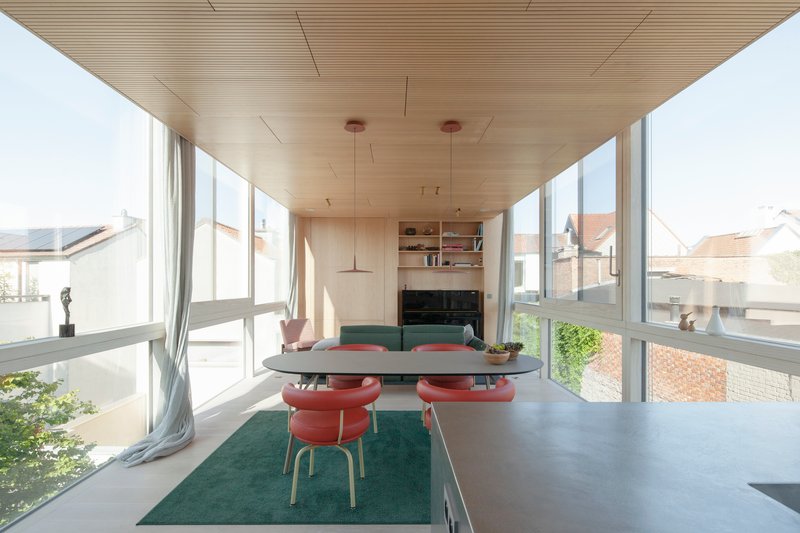 Open dining room with slatted timber ceiling, full-height glazing and red pendant lights in afternoon sun
