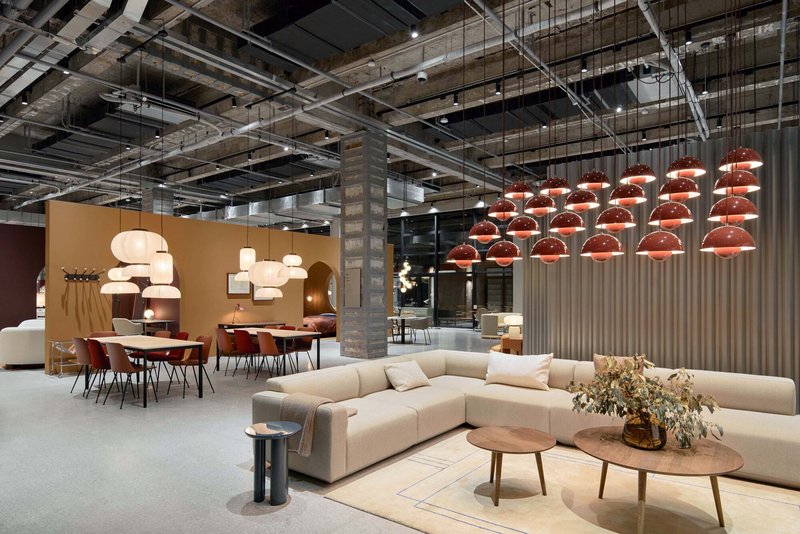 Showroom floor with sectional sofas, dining displays, and copper pendant lights beneath exposed structural ceiling