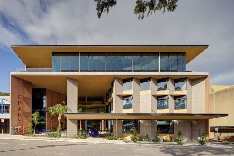 Street view of the cantilevered facade with timber soffits and full-height glazing under cloudy skies