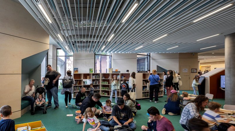 Library space with linear metal ceiling baffles and children seated on green carpet reading