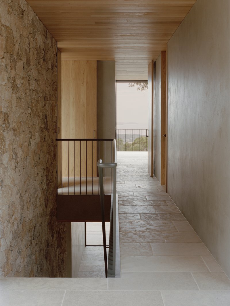Upper-level hallway with stone feature wall and steel balustrade overlooking the floor below