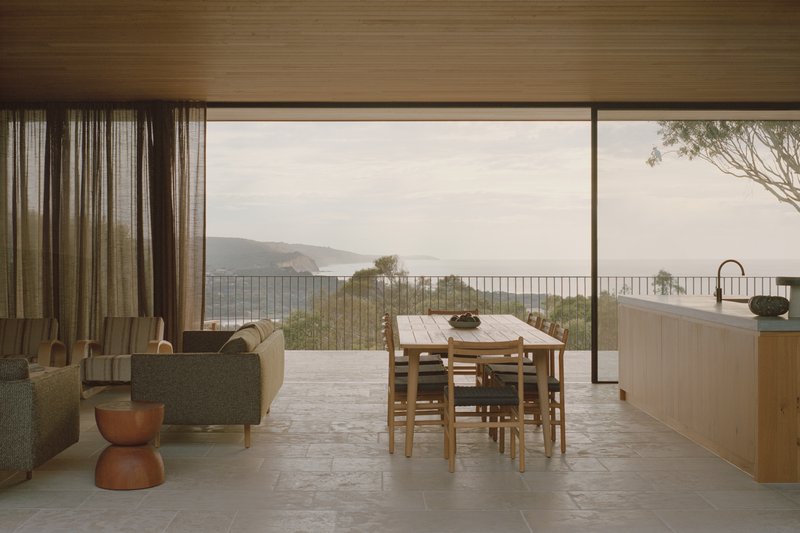 Open-plan living and dining space with full-height glazing opening to a coastal terrace overlooking distant hills