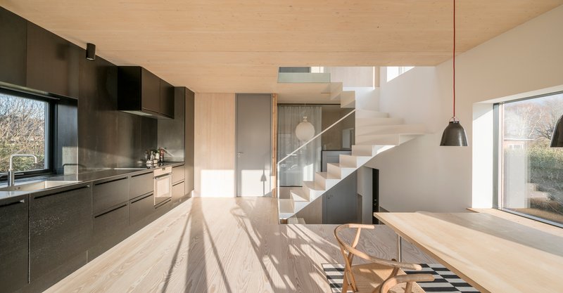 Open-plan kitchen and dining area with plywood ceiling and staircase bathed in afternoon sunlight