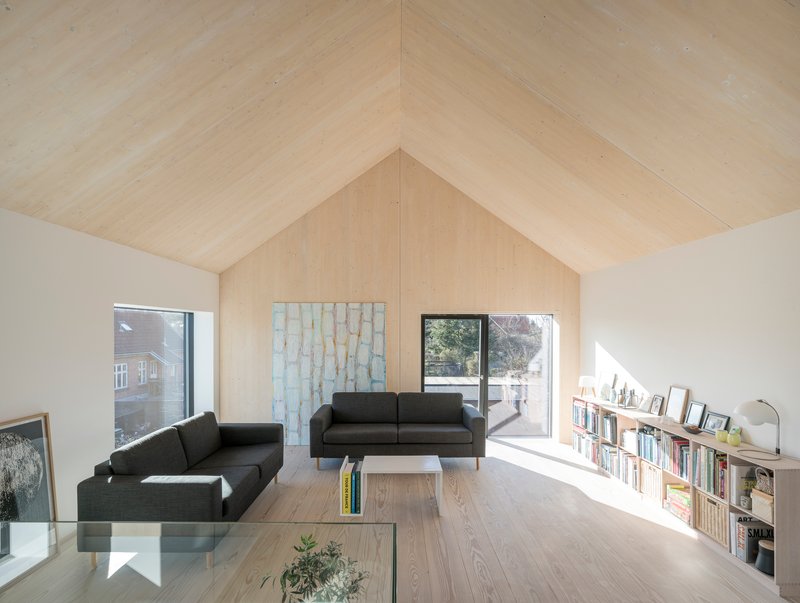 Living room with vaulted plywood ceiling, low bookshelf and framed view to outdoor terrace