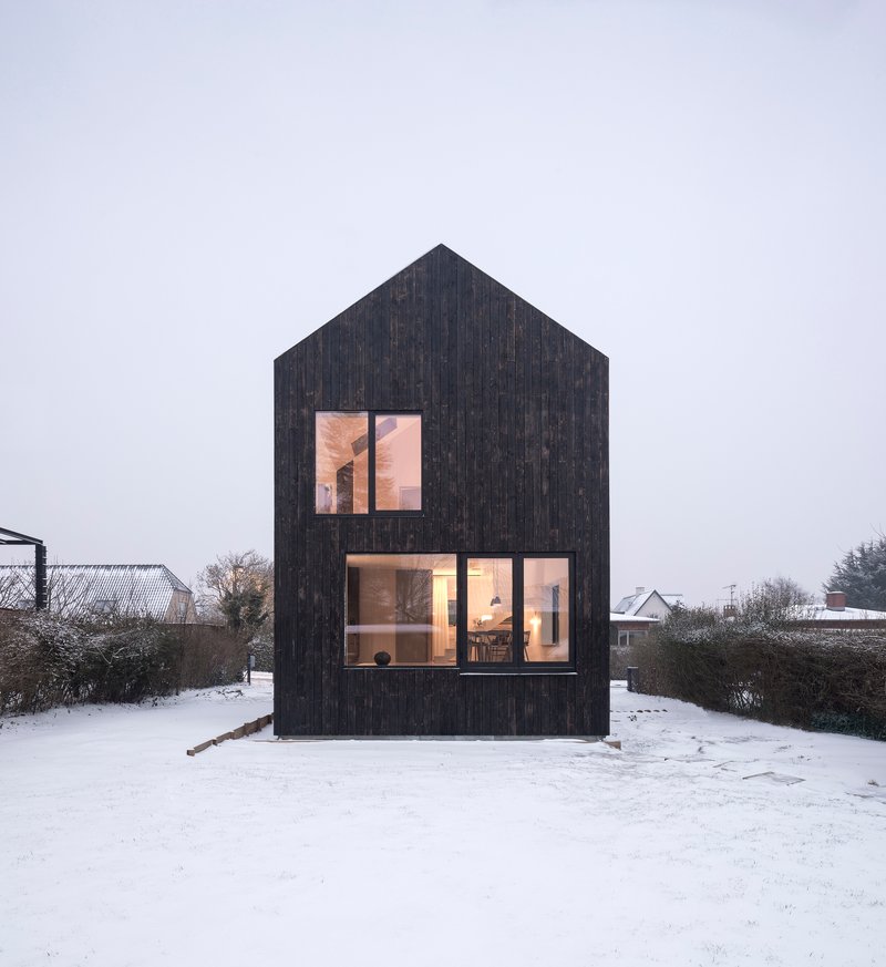 Gable-fronted elevation with charred timber cladding and large glazed openings in a snowy landscape