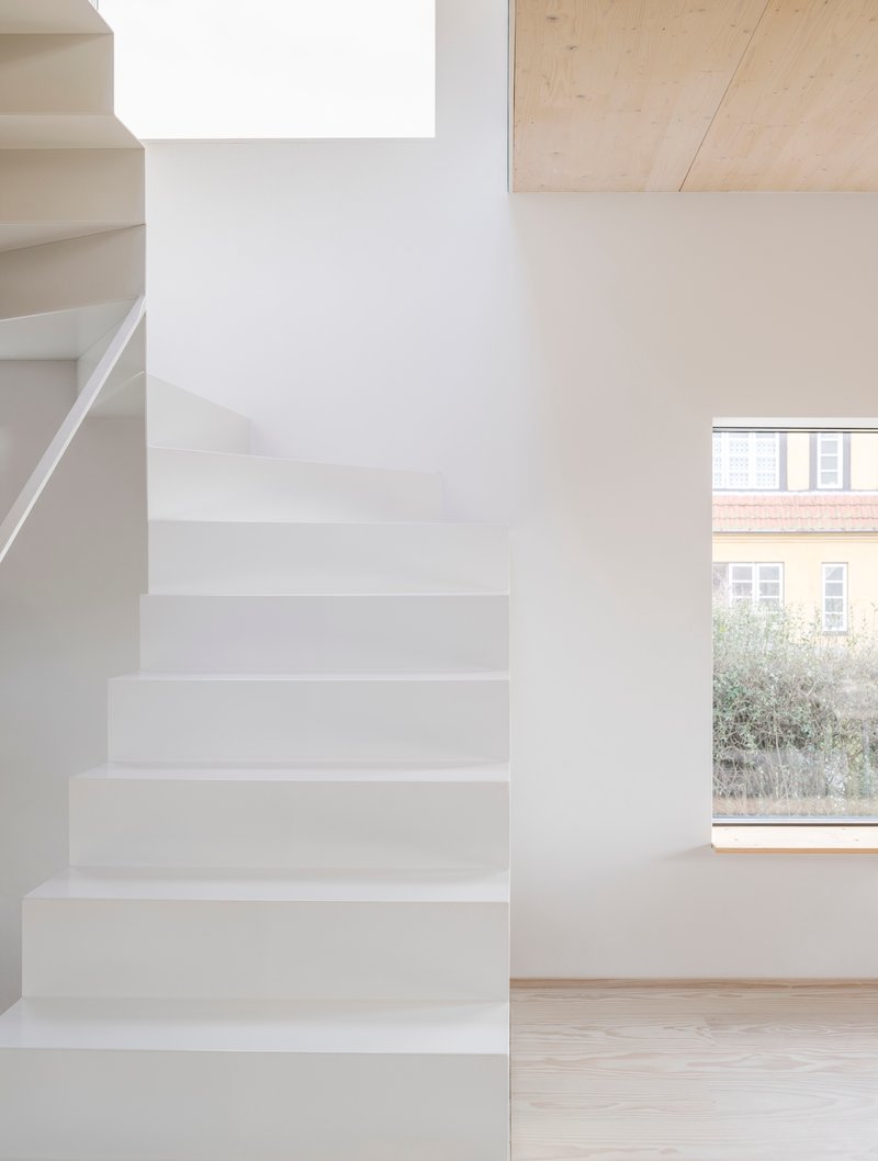 White plastered staircase next to a window overlooking neighboring brick buildings