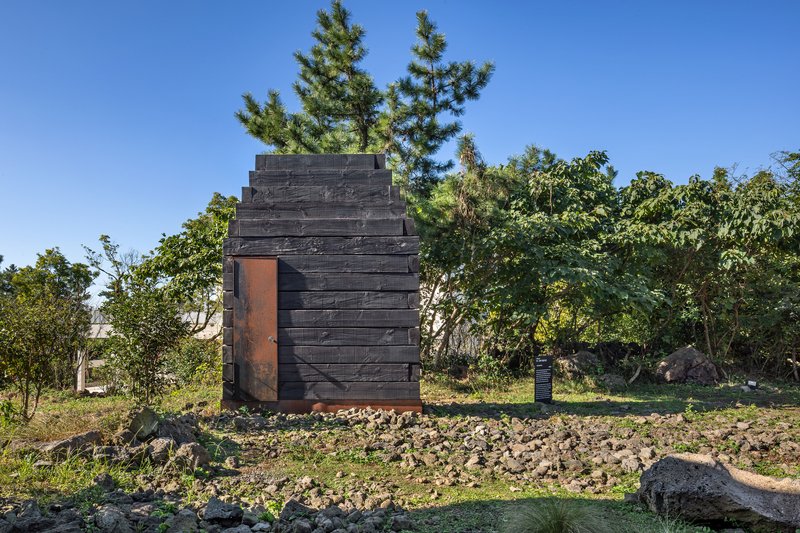 Stepped timber tower clad in charred wood with weathered steel door set in grassy clearing