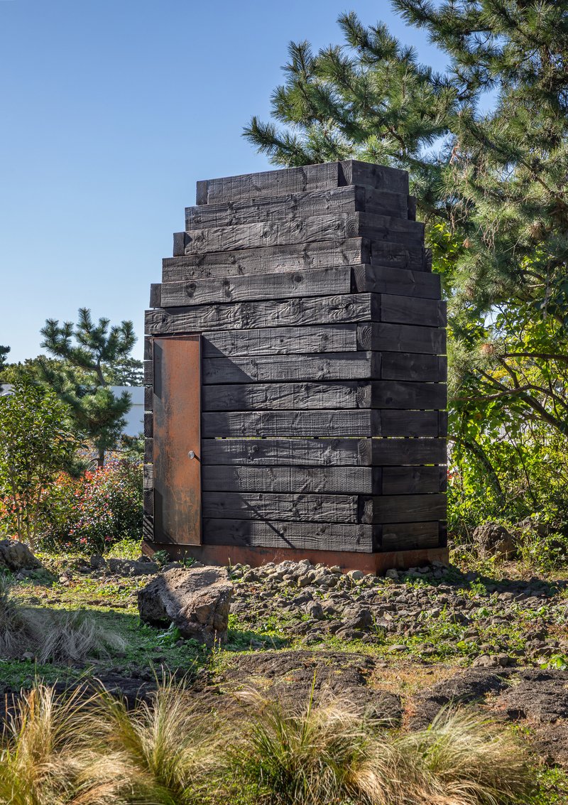 Charred timber facade with stepped profile and weathered steel doorway amid pine trees