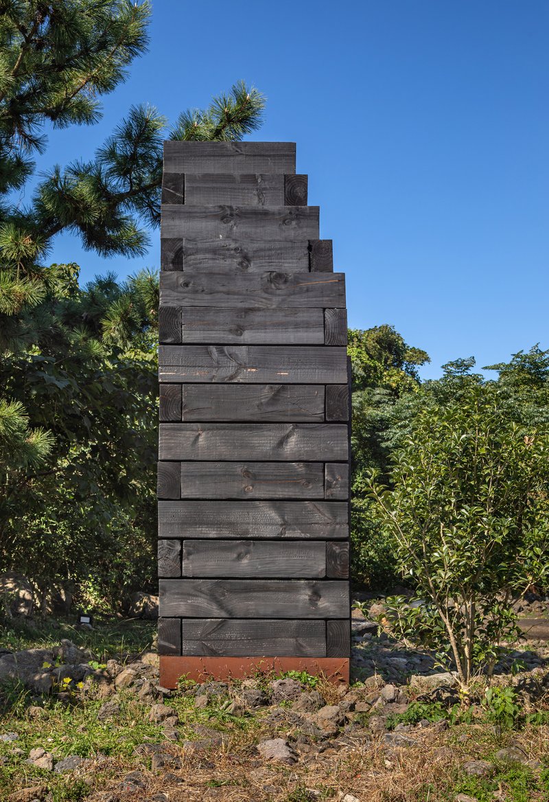Rear view of charred timber tower with horizontal planks and weathered steel base