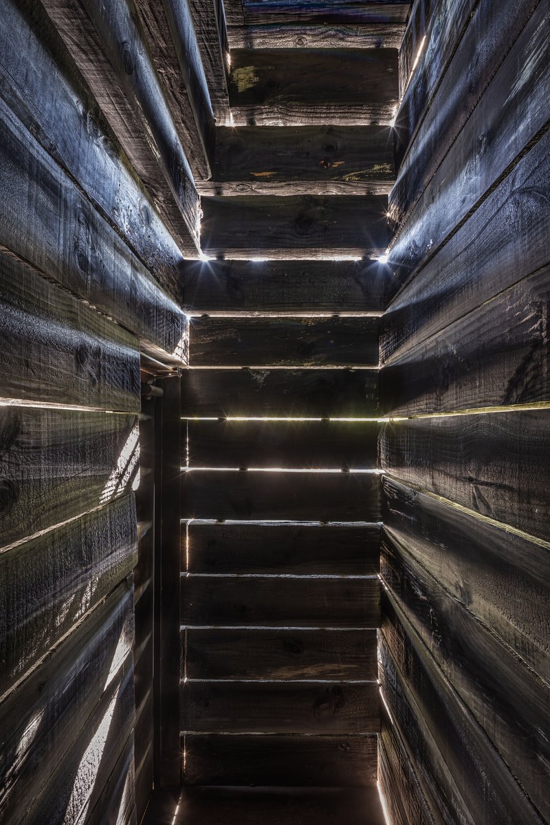 Interior view looking up through vertical shaft with horizontal timber slats and light filtering through