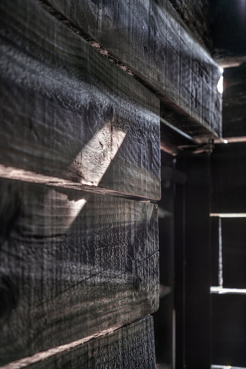 Close-up of charred timber beams with horizontal gaps allowing daylight to penetrate through the structure
