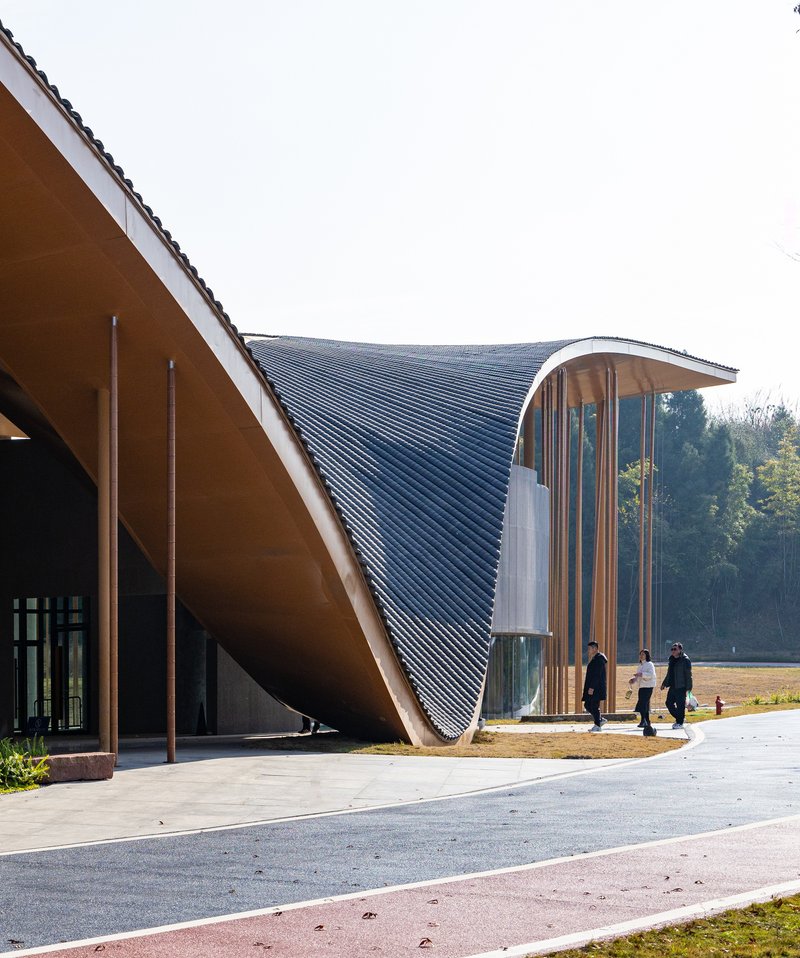 Entrance facade showing the swooping roof soffit and vertical tube screen with visitors walking beneath