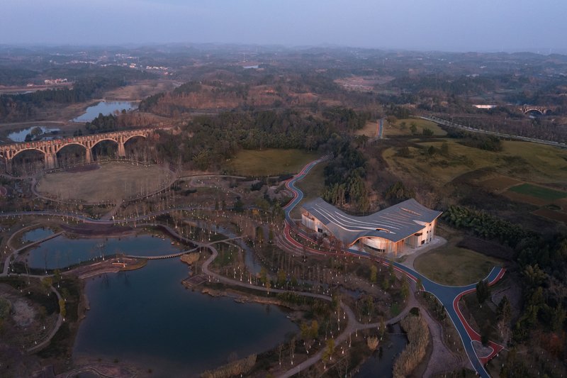 Drone view of the undulating roof building set among pathways and water features at dusk
