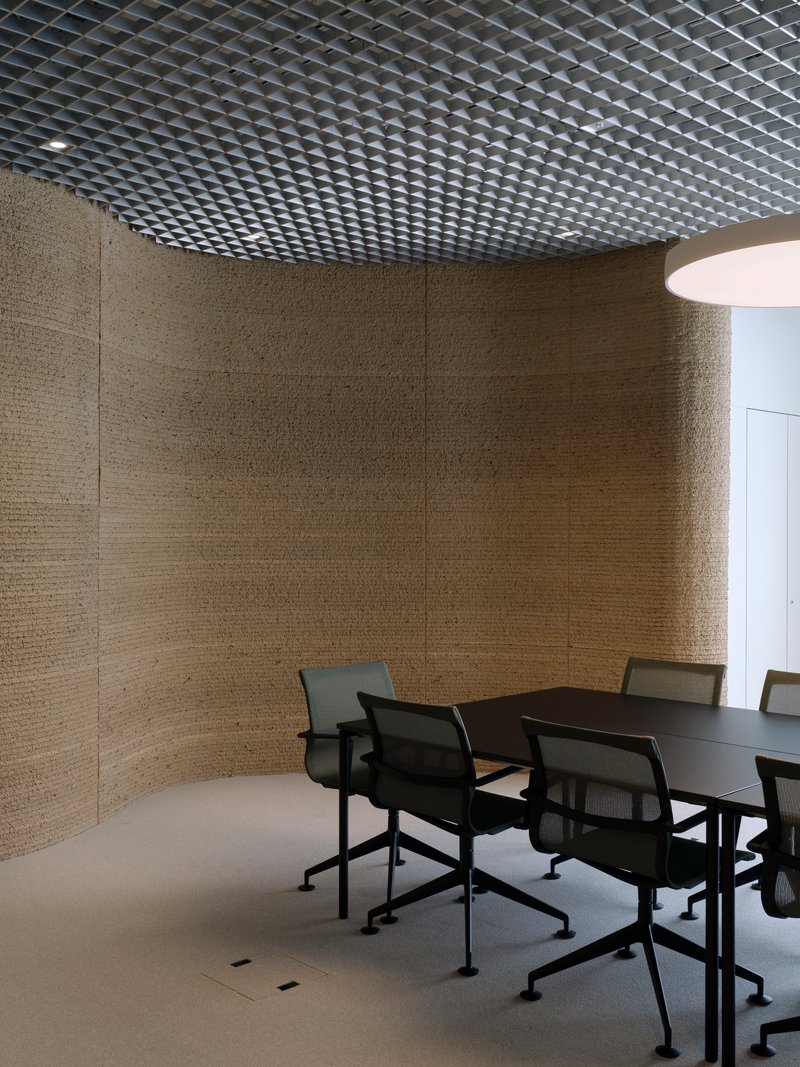 Meeting room with curved textured wall panels and perforated metal ceiling beneath diffused light