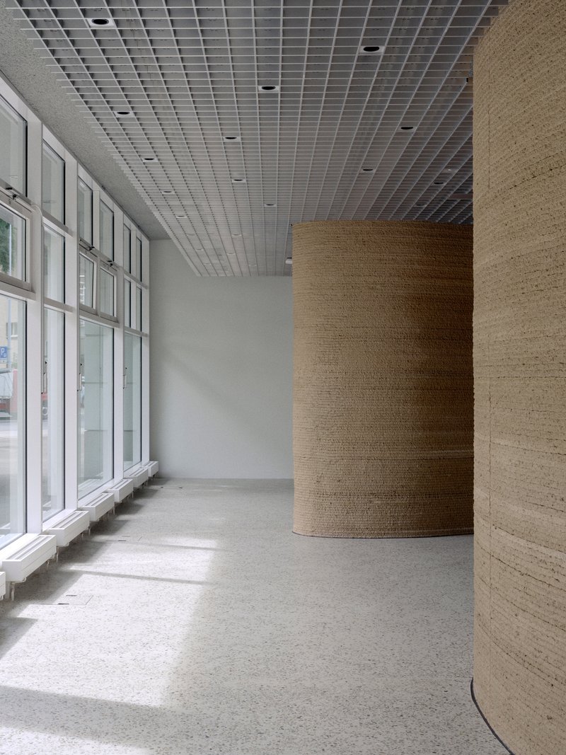 Curved timber-wrapped columns flanking glazed facade with filtered daylight on terrazzo floor