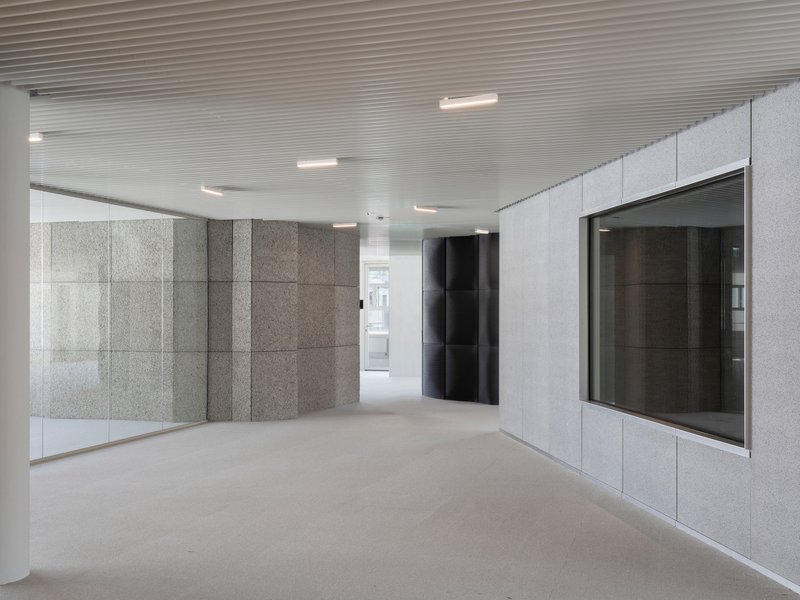 Lobby space with textured grey stone wall panels, black elevator doors, and ribbed metal ceiling with recessed lighting