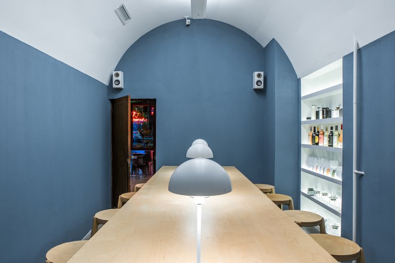 Arched blue wall framing a plywood table with pendant lamp and backlit shelving alcove