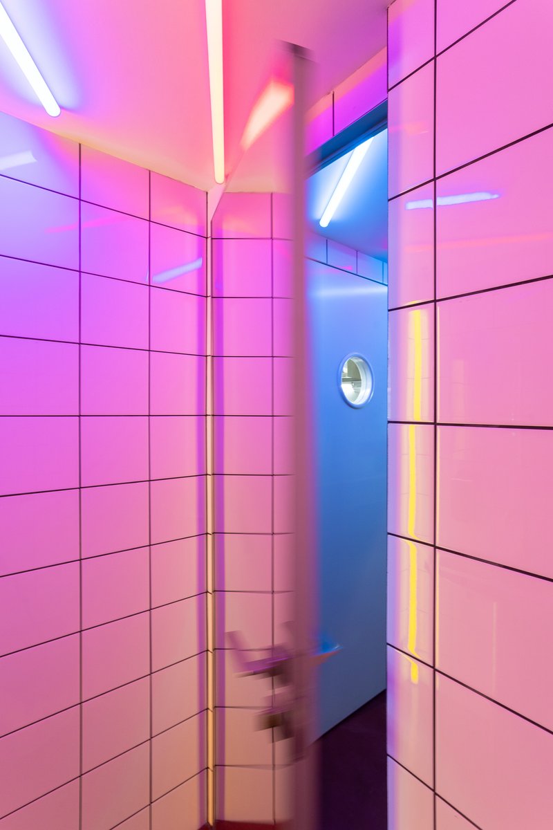 Tiled hallway with pink and blue neon lighting and motion-blurred figure passing through