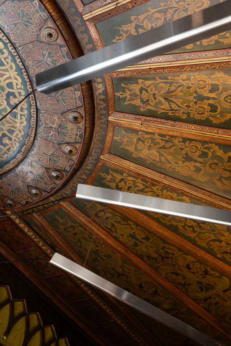Detail of painted ceiling panels with gilded borders and decorative foliate patterns between timber beams
