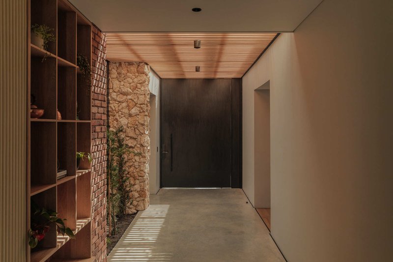 Interior hallway with timber slatted ceiling, brick wall, stone wall and wooden shelving catching afternoon light