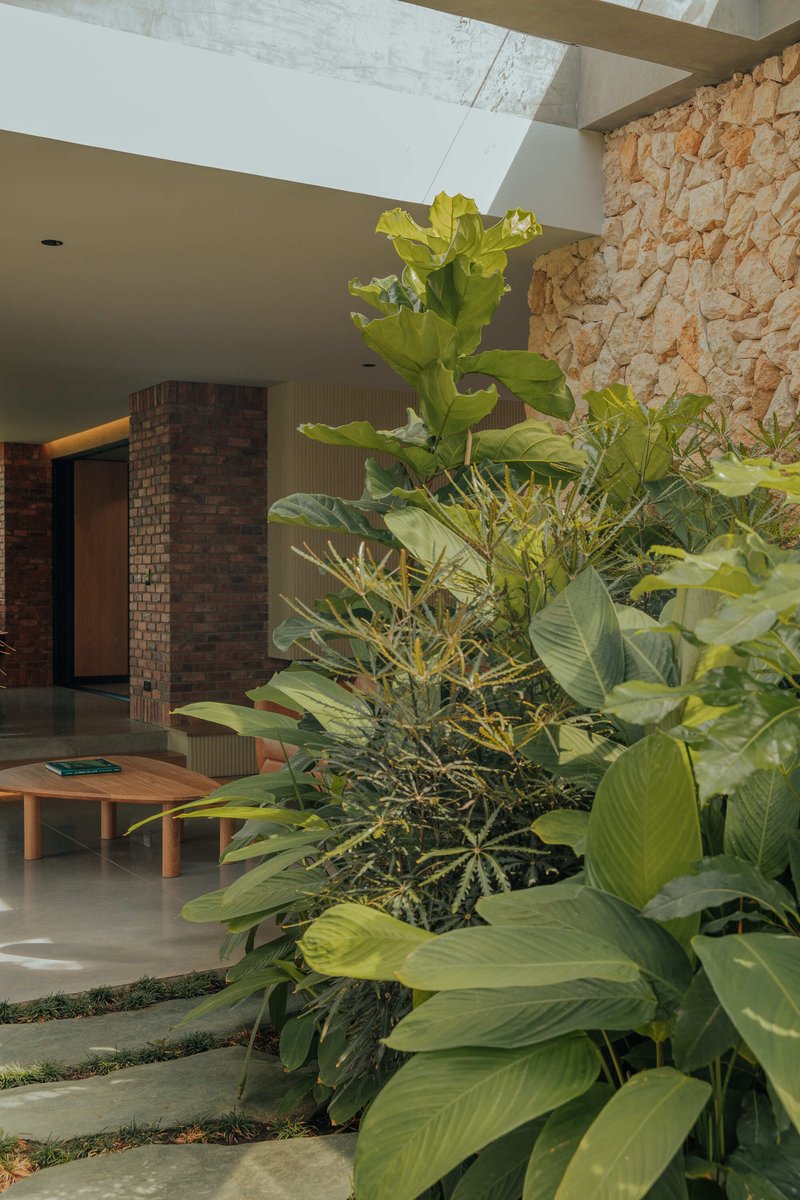 Covered courtyard with concrete floor, limestone wall and planted tropical foliage under flat ceiling