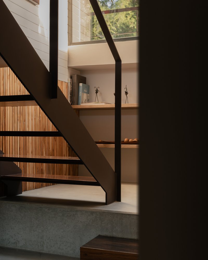 Steel staircase with shadow patterns cast across concrete treads and slatted timber wall in afternoon light