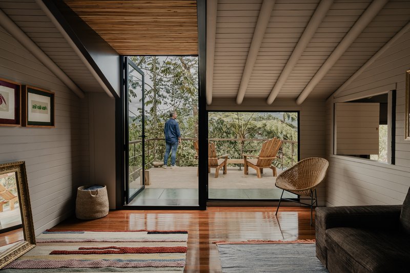 Bedroom opening to deck with timber chairs as figure stands among surrounding eucalyptus trees