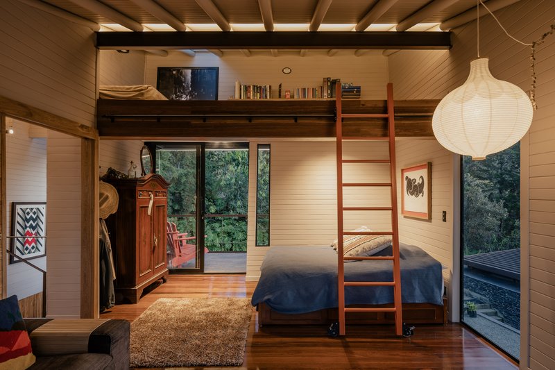 Bedroom with loft accessed by timber ladder and paper pendant light beside forest-facing windows