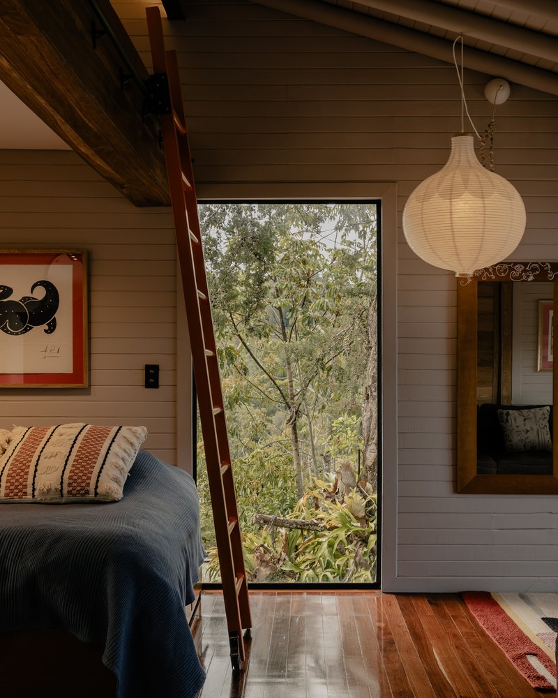 Floor-to-ceiling window framing eucalyptus trees beside a bed and paper lantern